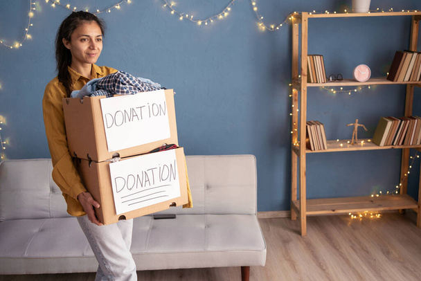 Concetto di donazione. Donna che regge scatole di donazioni con vestiti in piedi a casa. Donazione di vestiti. Copia spazio - Foto, immagini