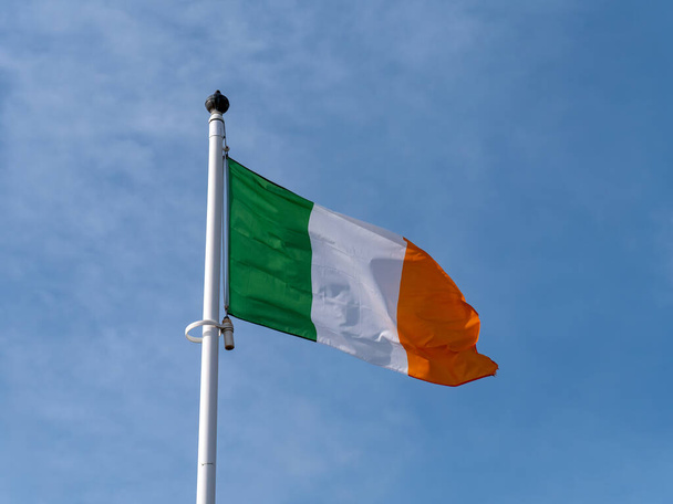 Один флаг Ирландии на флагштоке против голубого неба. - Фото, изображение