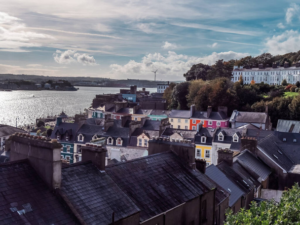 Uitzicht op het kleine Ierse kustplaatsje Cobh, stedelijk landschap. Avondlucht boven de stad. Europese stedelijke architectuur. Luchtfoto van stadsgebouwen in de buurt van het waterlichaam. Daken van huizen. - Foto, afbeelding