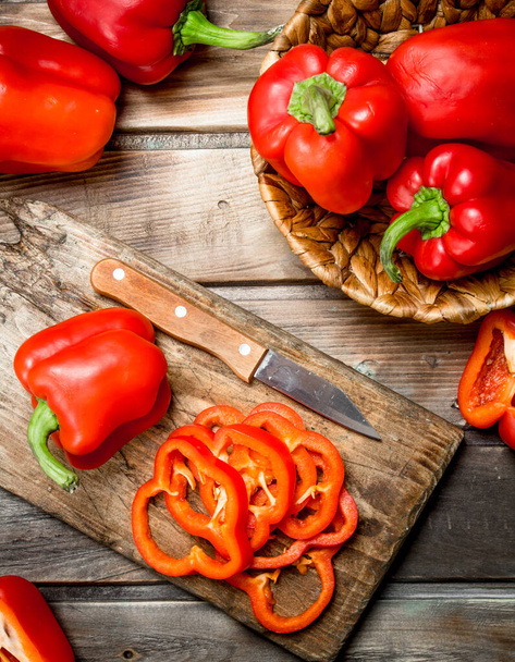 Sliced sweet pepper on a cutting Board with a knife and ripe pepper in a basket. On wooden background - Foto, afbeelding