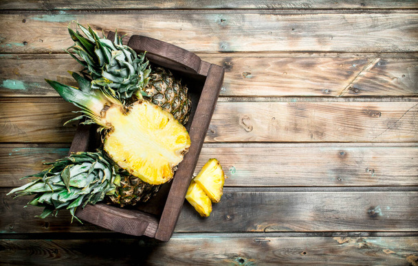 Half and whole pineapples in the box. On wooden background - Zdjęcie, obraz