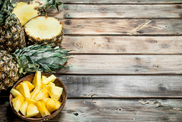 Slices of pineapple in a bowl and fresh pineapple. On wooden background - Fotoğraf, Görsel