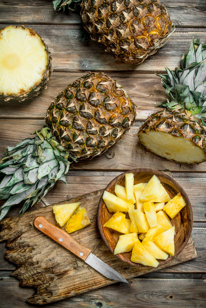 Sliced pineapple in a bowl on a cutting Board with a knife and a whole pineapple. On wooden background - Foto, afbeelding