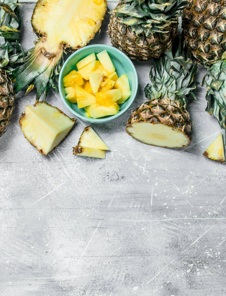 Pieces of fresh pineapple with greens and sliced pineapple in bowl. On rustic background - Foto, Imagem