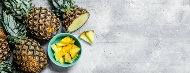 Pieces of fresh pineapple in a bowl and ripe pineapples. On white rustic background - Fotografie, Obrázek