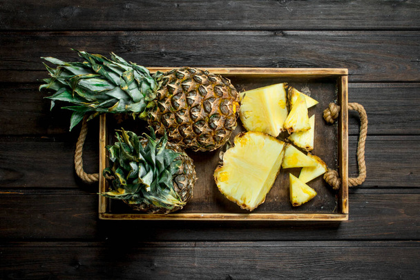 Whole and slices of ripe pineapple on a tray. On wooden background - Foto, Imagem