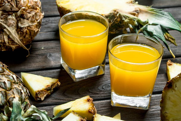 Pineapple juice in a glass and pieces of fragrant pineapple. On wooden background - Photo, Image