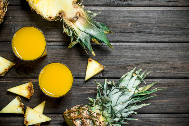 Pineapple juice in a glass and pieces of fragrant pineapple. On wooden background - Photo, image