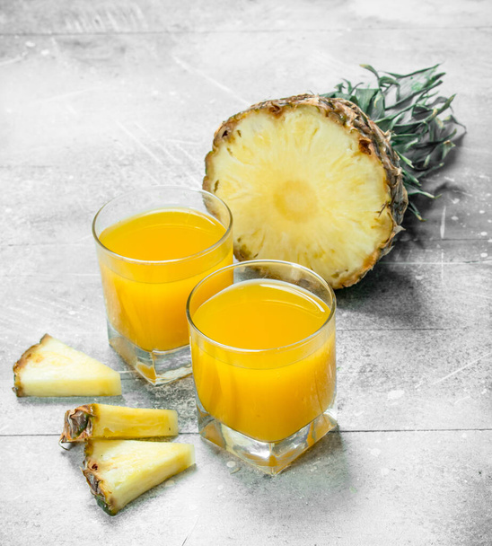 Pineapple juice in a glass and slices of ripe pineapple. On white rustic background - Фото, изображение
