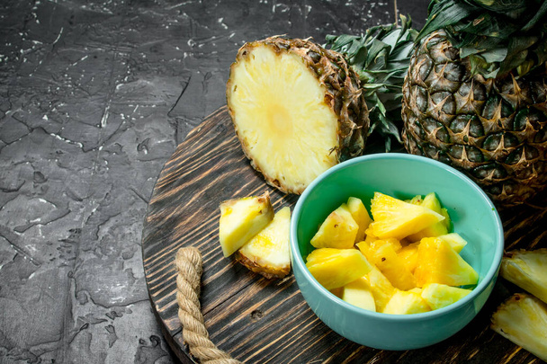 Cut fresh pineapple in bowl on tray. On black rustic background - Foto, afbeelding