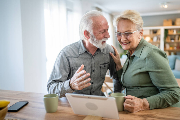 Yaşlı bir çift, Kafkasyalı yaşlı bir adam ve bir kadın, emekli bir koca ve bir büyükanne, dijital tablet kullanarak evlerinde video çekiyor. Parlak bir odada, gerçek insanlar, aile kavramını taklit ediyorlar. - Fotoğraf, Görsel