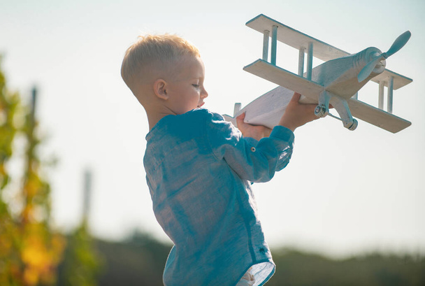 Child pilot with toy airplane dreams of traveling in summer in nature. Kids dreams. Child plays with a toy plane and dreams of becoming a pilot. Childhood dream imagination concept - Foto, Imagem