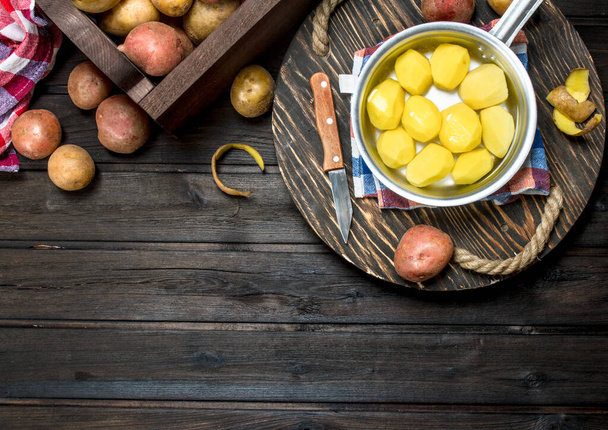 Potatoes in a saucepan with napkin and a knife on tray. On wooden background - Foto, afbeelding