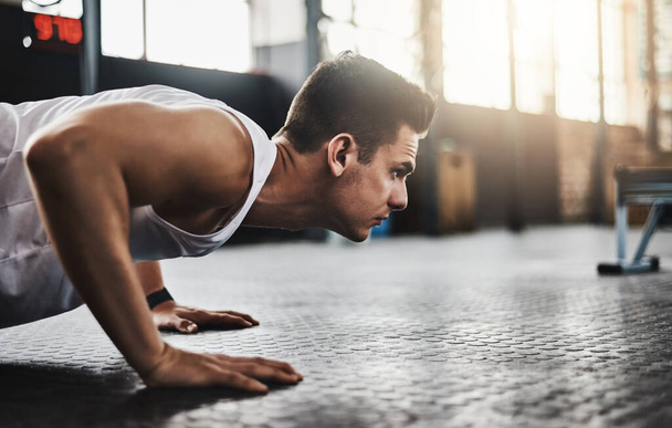 A fitnesz a koncentráltaké. Egy fiatal férfi fekvőtámaszt csinál egy edzőteremben. - Fotó, kép