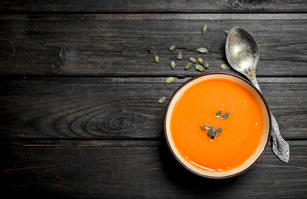 Pumpkin soup in bowl with spoon. On black wooden background - Foto, Bild