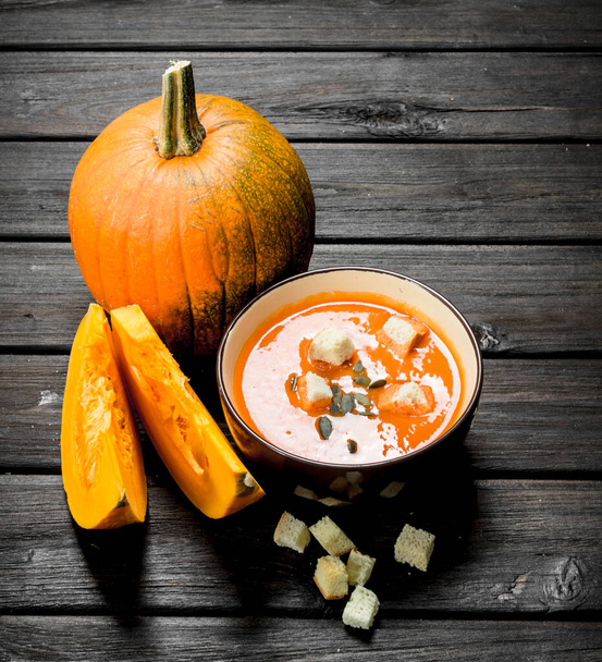 Pumpkin soup in bowl with rusks and whole pumpkin. On wooden background - Fotografie, Obrázek