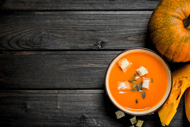 Pumpkin soup in bowl with rusks and whole pumpkin. On wooden background - Fotoğraf, Görsel