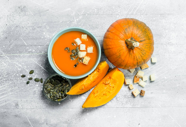 Pumpkin soup with slices of ripe pumpkin and seeds. On white rustic background - Фото, изображение
