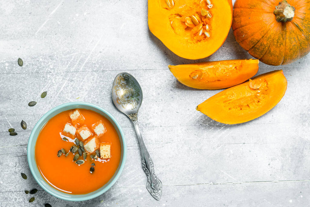 Pumpkin soup in a bowl with a spoon and pieces of fresh pumpkin. On rustic background - Fotografie, Obrázek