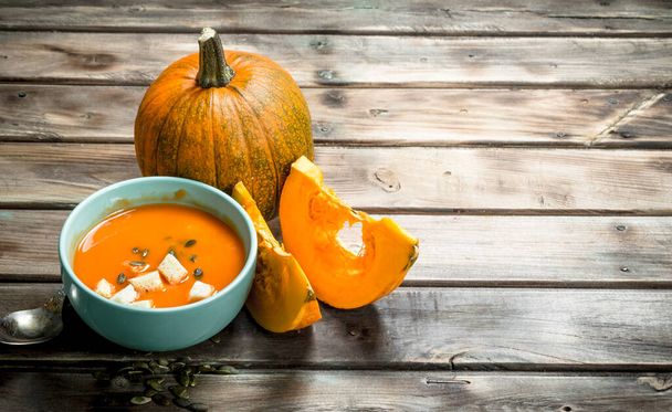 Pumpkin soup in bowl with spoon and fresh pumpkin. On wooden background - Fotoğraf, Görsel