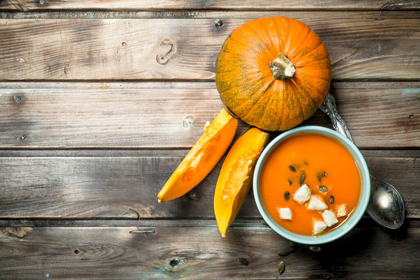 Pumpkin soup in bowl with spoon and fresh pumpkin. On wooden background - Фото, зображення