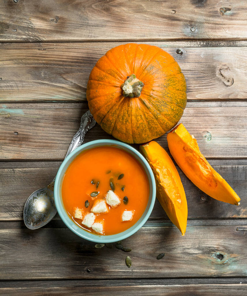 Pumpkin soup in bowl with spoon and fresh pumpkin. On wooden background - Foto, afbeelding