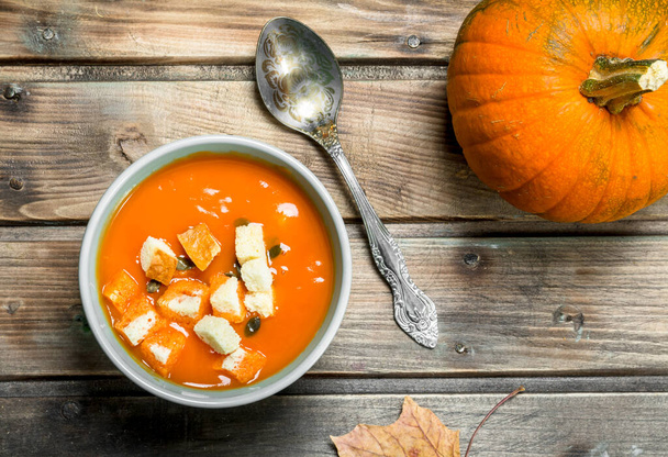 Pumpkin soup in a bowl with a spoon and a whole pumpkin. On wooden background - Fotoğraf, Görsel