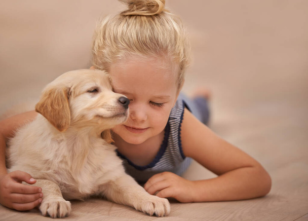 Young girl hug her dog, relax with peace and calm at home with golden retriever puppy and child. Mans best friend, pet care and love with female kid and her domestic animal lying on wood floor. - Photo, Image