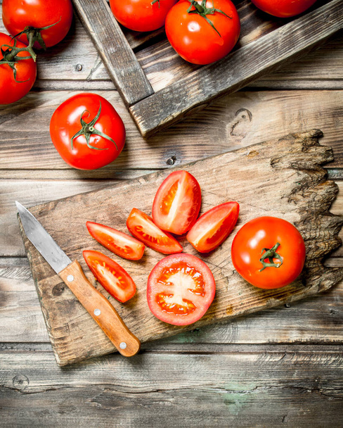 Cut tomatoes on a cutting Board with a knife. On wooden background - Zdjęcie, obraz