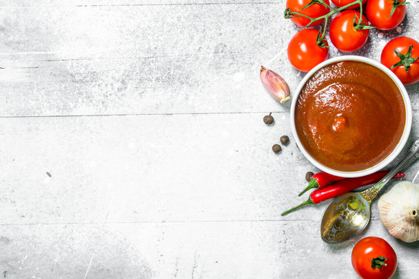 Tomato sauce in bowl with spoon, garlic and cherry. On rustic background - Valokuva, kuva