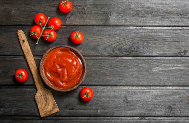 Tomato sauce in bowl with wooden scoop and cherry. On wooden background - Zdjęcie, obraz