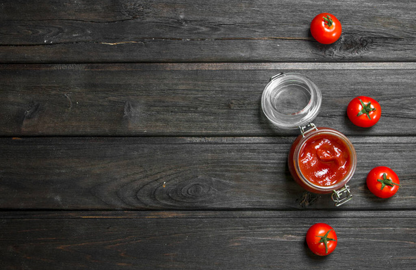 Tomato sauce in a glass jar and fresh tomatoes. On wooden background - Foto, Imagen