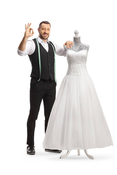 Tailor standing next to a bridal gown on a doll mannequin and gesturing great isolated on white background - Foto, imagen