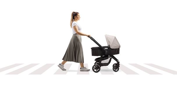 Full length profile shot of a young mother pushing a stroller and crossing street isolated on white background - Foto, imagen