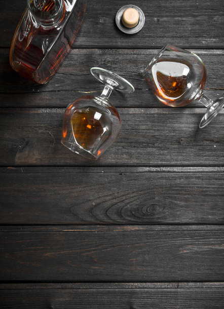 Cognac in a glass bottle and glasses. On black wooden background - Fotoğraf, Görsel