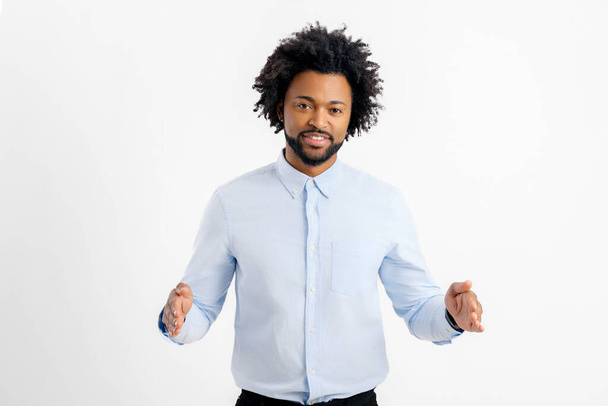 Smiling Aferican-American young man holding two hands in front of him and shows the wide size, curly guy in white shirt advertising novelty, presenting some product isolated on white background - Φωτογραφία, εικόνα