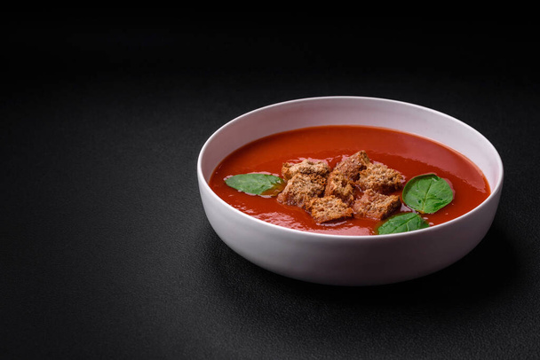 Delicious fresh gazpacho with breadcrumbs, salt and spices in a ceramic plate on a dark concrete background - Foto, Bild