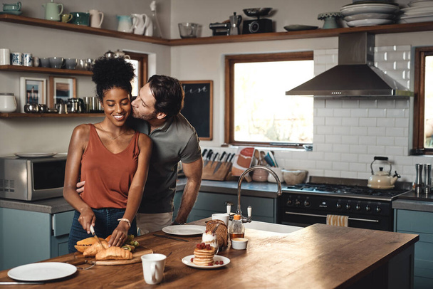 Межрасовая пара, поцелуй и приготовление завтрака на кухне на утро, любовь или забота в браке дома. Счастливый мужчина целует женщину для еды, питания или объятий в счастье для здоровых отношений. - Фото, изображение
