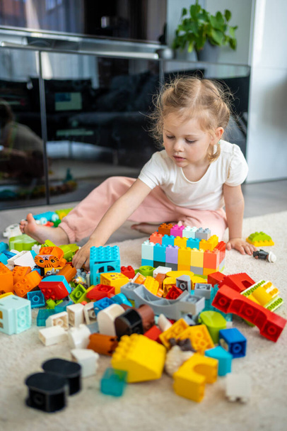 Kleine Mädchen spielen mit Konstrukteursspielzeug auf dem Fußboden im Haus, Lernspiel, verbringen Freizeitaktivitäten Zeitkonzept. Hochwertiges Foto - Foto, Bild