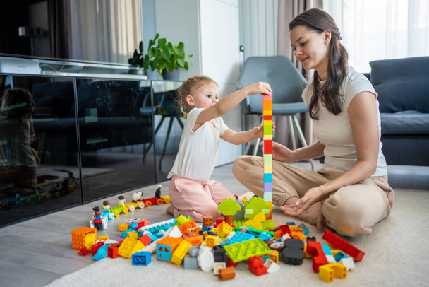 Pieni tyttö leikkiä rakentaja lelu lattialla kotona äidin tai naisen lapsenvahti, opettavainen peli, perhe kotona viettää vapaa-aikaa yhdessä käsite. Laadukas kuva - Valokuva, kuva