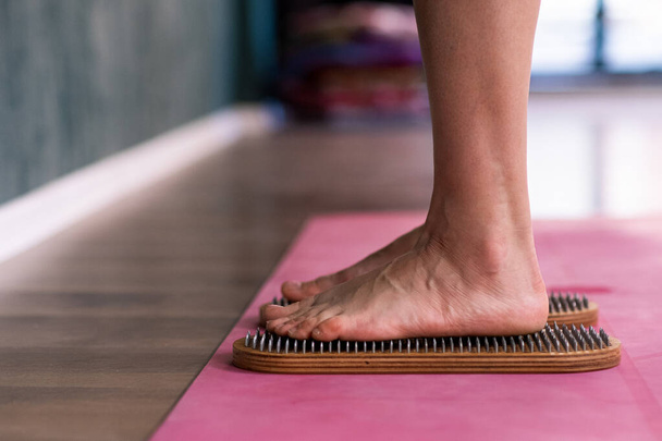 Standing barefoot woman doing nail reflexotherapy at professional yoga class feet of female person on sadhu boards on pink mat in spacious studio effective body relaxation practice closeup - Foto, afbeelding