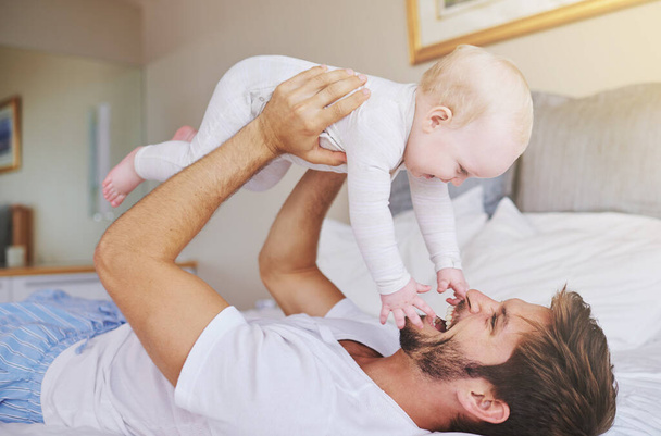 Father, on bed and play with baby girl up in the air or flying daughter and having fun in the bedroom feeling happy. Parent, kid and dad bonding or carefree and excited together in the house. - Foto, imagen