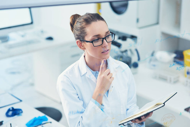 I have to think about that for a second. a focused young female scientist reading from her notebook while contemplating inside of a laboratory - Photo, Image