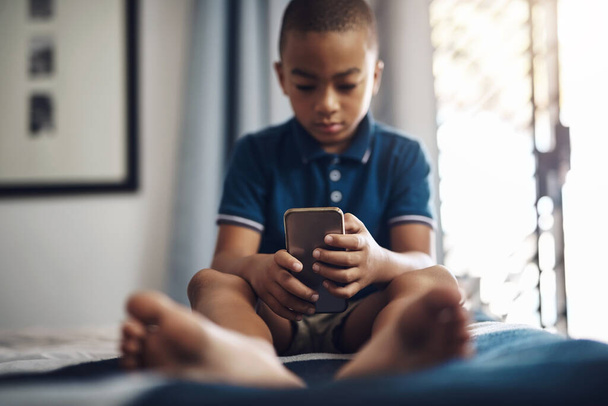 Mogą dowiedzieć się więcej o wszystkim w sieci. młody chłopiec korzystający z telefonu komórkowego siedząc na łóżku - Zdjęcie, obraz