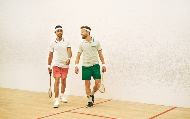 No sólo compañeros de equipo, son los mejores amigos. dos hombres jóvenes charlando después de jugar un juego de squash - Foto, imagen