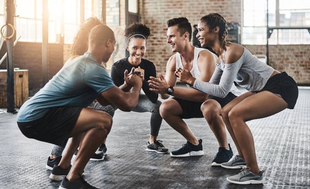 Onderlichaam kracht met dank aan de squat training. een groep jongeren die samen hurken tijdens hun training in een fitnessruimte - Foto, afbeelding