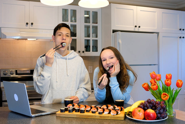 delicious sushi learn to eat with chopsticks show each other master class on cooking japanese asian food properly hold chopsticks fool around play boy and girl teenagers in kitchen watching a movie - Photo, Image