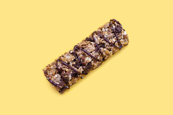 Muesli bar on a yellow background in the center. Whole grain energy bar with chocolate. Healthy food in the form of a sweet healthy bar. Healthy quick snack - Photo, Image