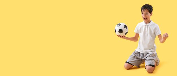 Niño feliz sosteniendo pelota de fútbol sobre fondo amarillo con espacio para el texto - Foto, imagen