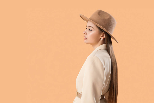 Modieuze jonge vrouw in stijlvolle jas en hoed op beige achtergrond - Foto, afbeelding